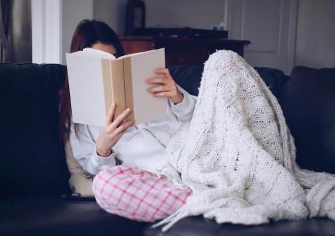 girl sitting in pajamas and a blanket, reading a book