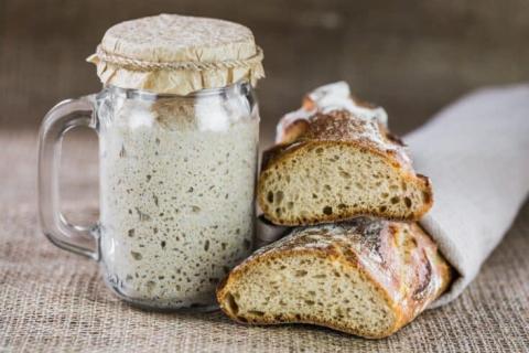 A photo of sourdough bread starter in a jar and two loaves of sourdough bread.