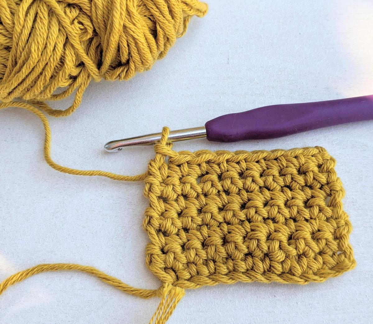 yellow yarn crocheted into a granny square with a purple hook.