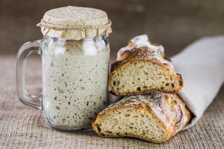 A photo of sourdough bread starter in a jar and two loaves of sourdough bread.
